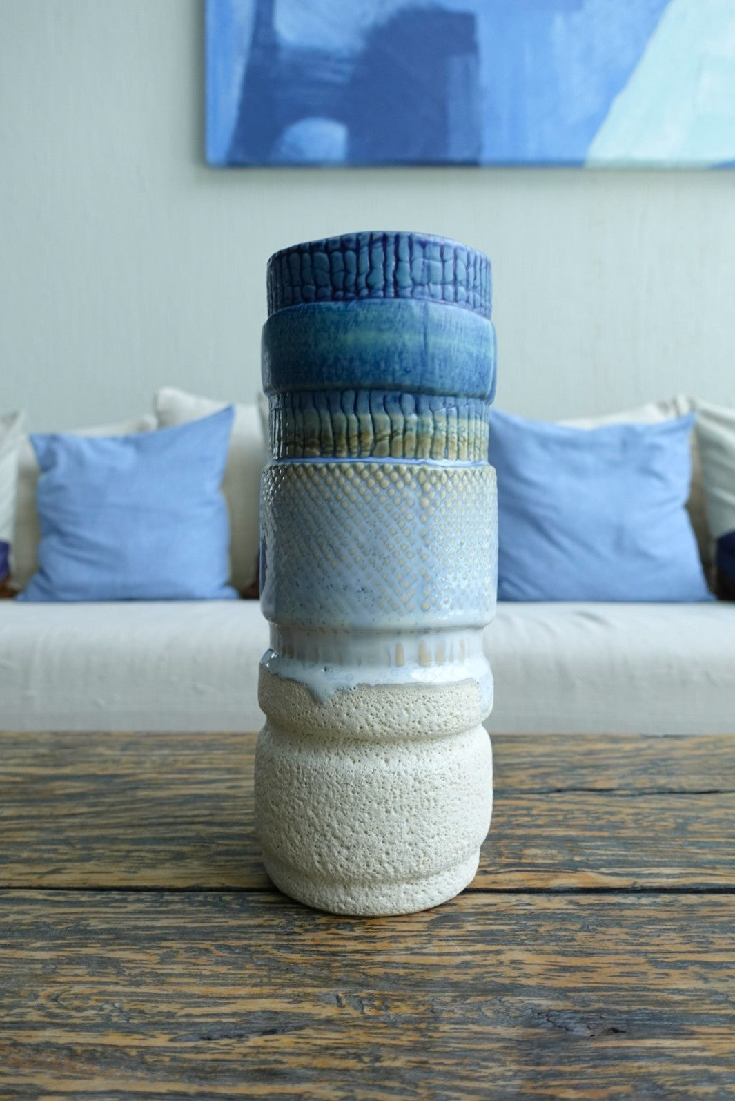 Textured ceramic vase on a wooden table with a couch and abstract painting in the background