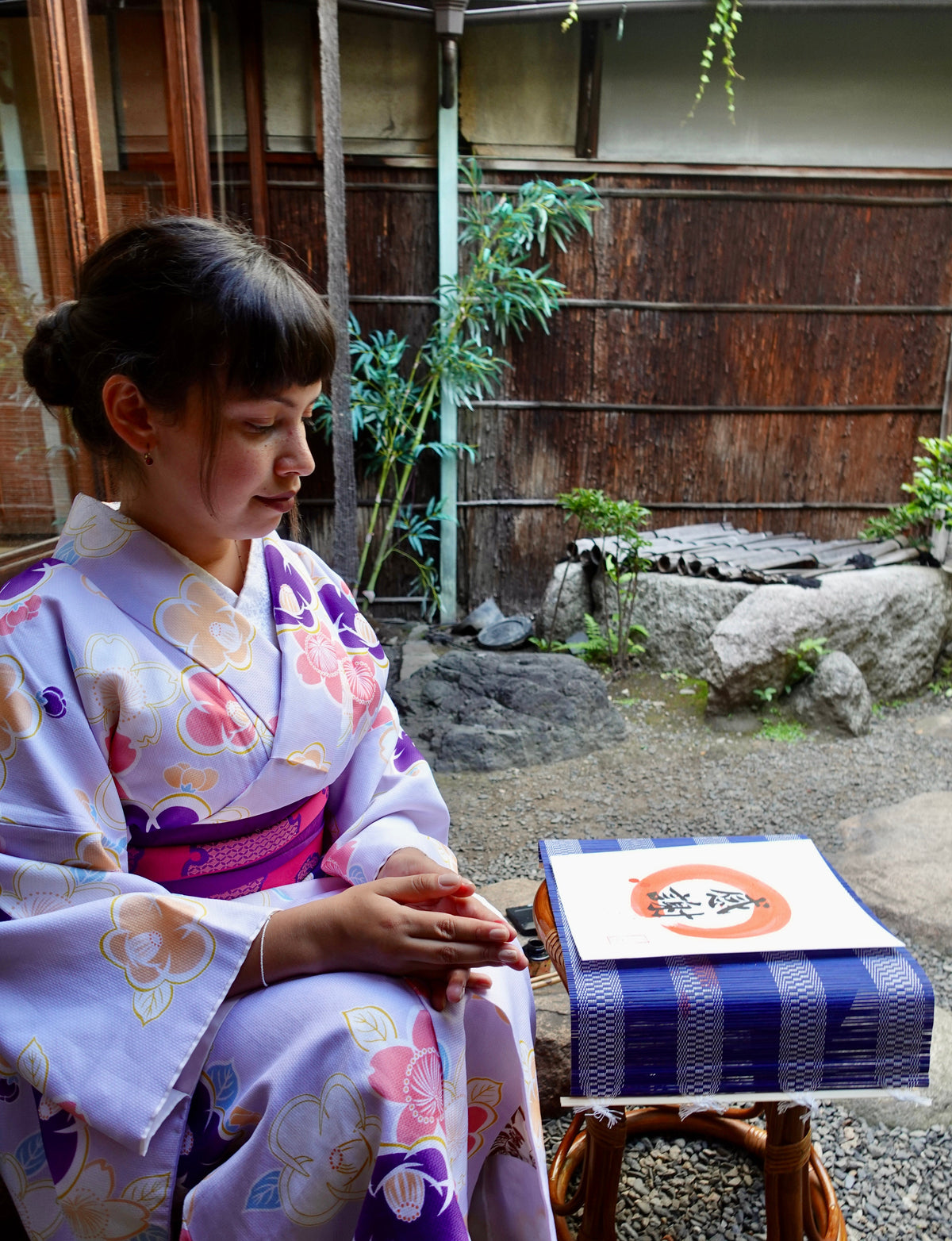 Woman in a traditional kimono sitting on a stone bench in a garden setting.