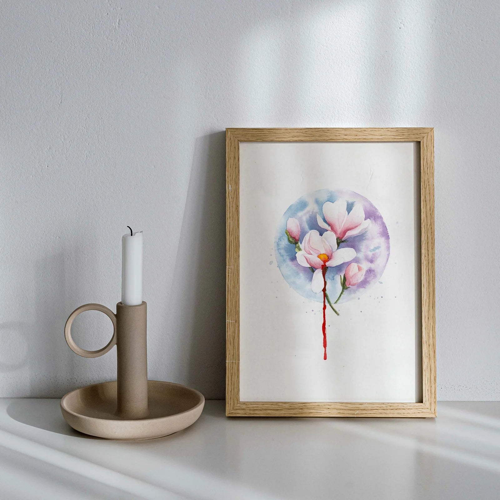 Framed floral artwork on a white surface with a candle and holder.