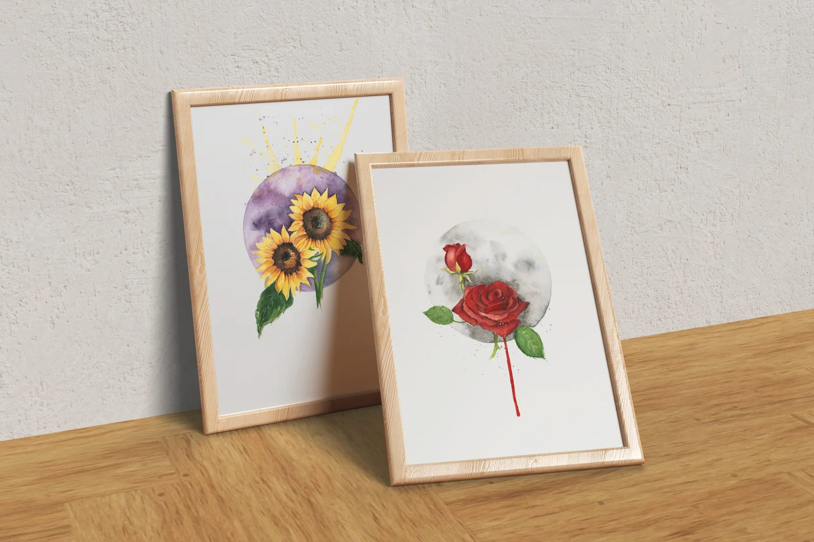 Two framed floral prints on a wooden surface with a light gray wall background