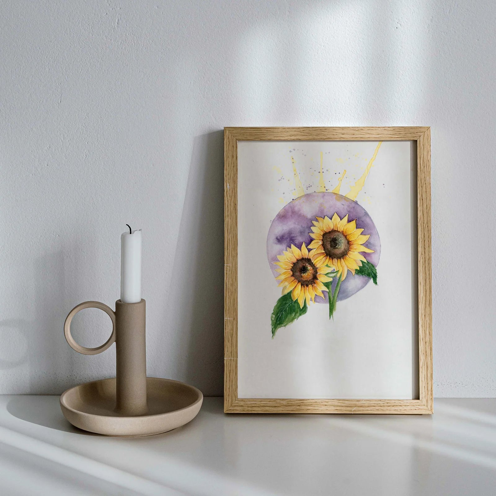 Framed artwork of sunflowers on a white surface with a candle holder.
