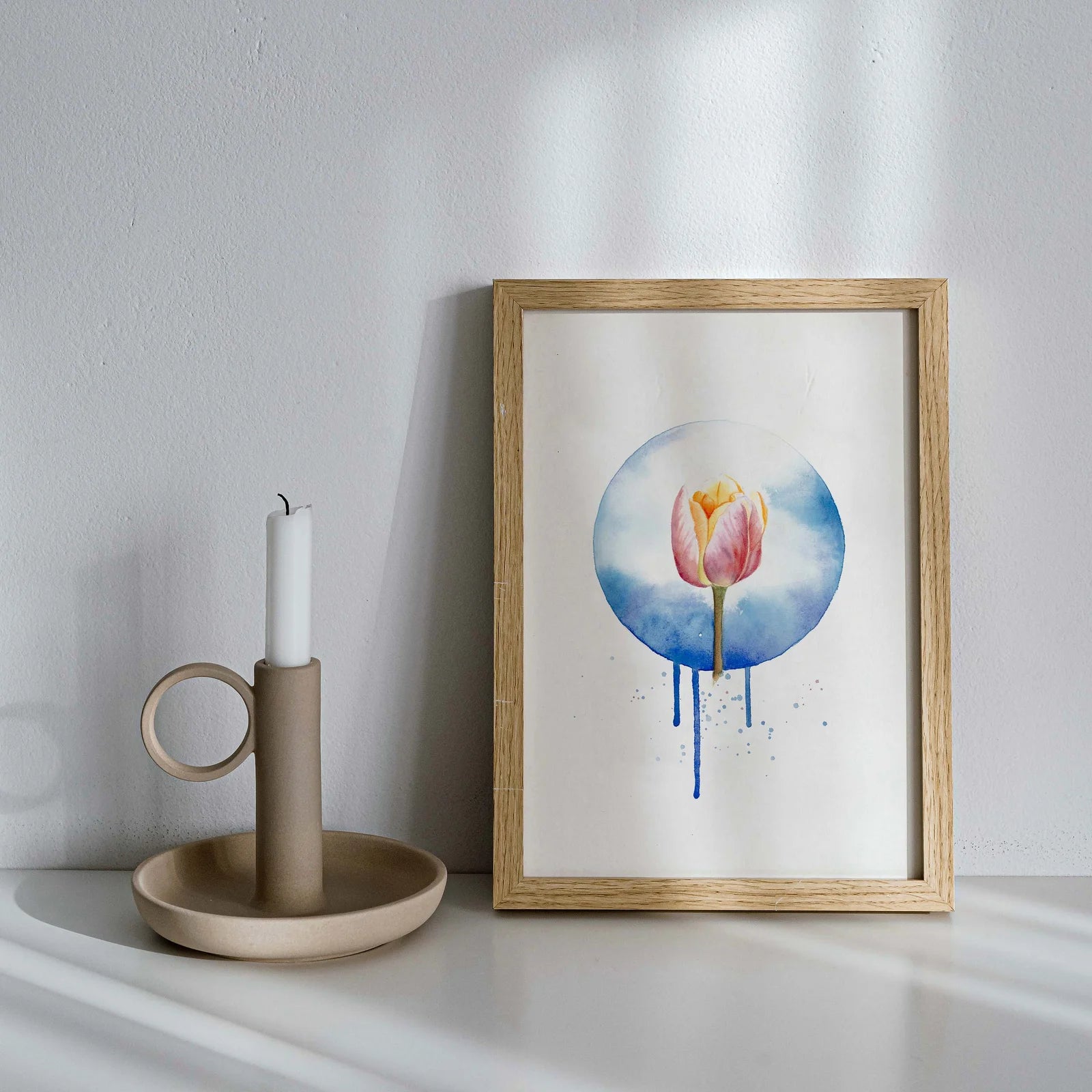 Framed artwork of a tulip with watercolor design on a white surface next to a candle holder.
