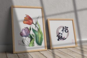 Framed watercolor artwork of colorful tulips, placed next to a framed Shodo calligraphy piece featuring black Japanese characters within a circular brushstroke. Both artworks are framed and positioned on a wooden floor with sunlight casting shadows against a wall.